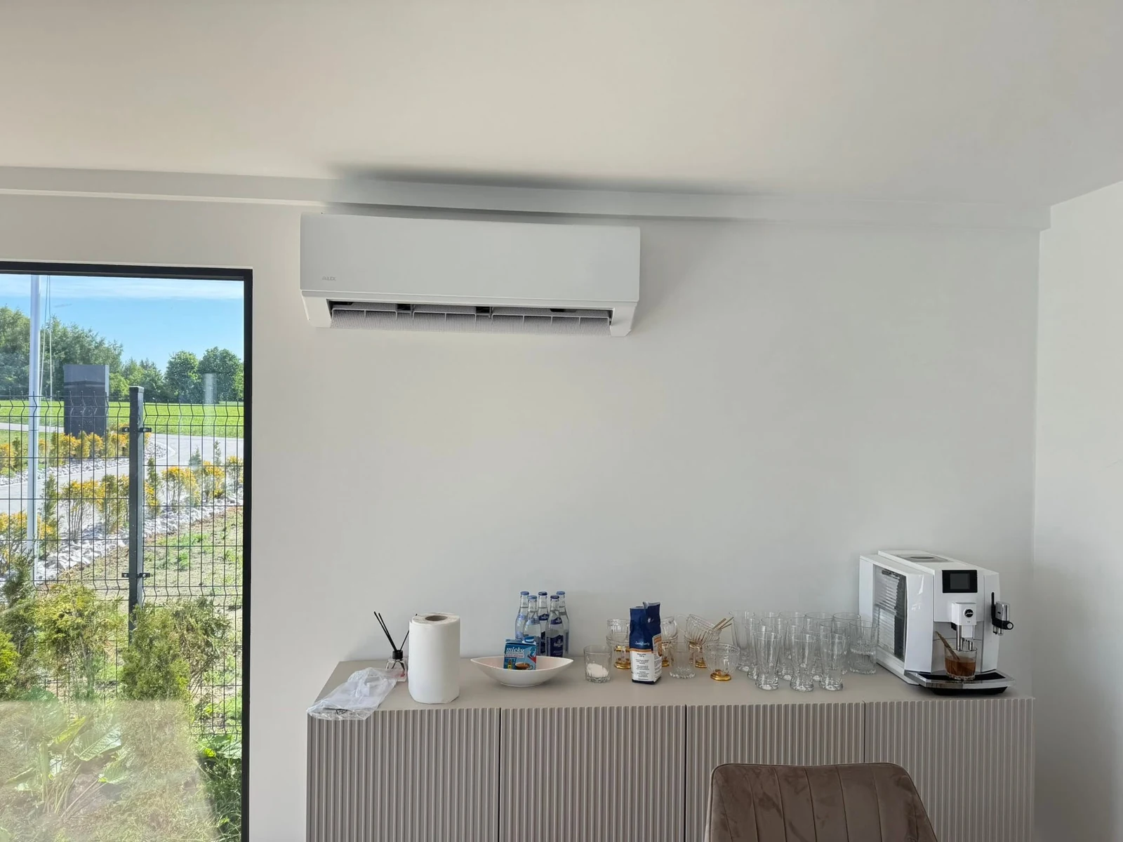 Biały klimatyzator ścienny nad szafką z ekspresem do kawy w jasnym biurze