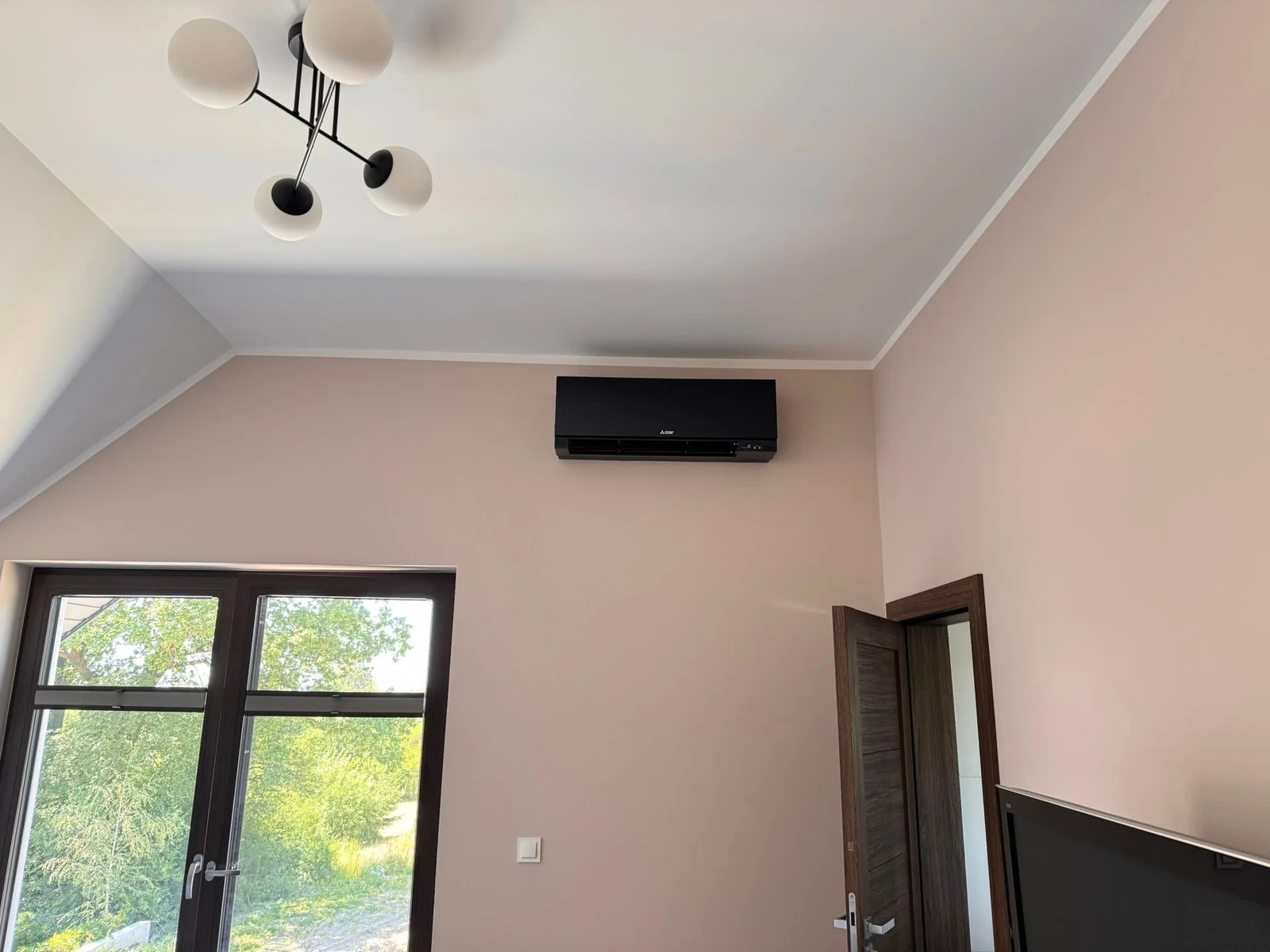 Czarny klimatyzator ścienny Mitsubishi Electric nad drzwiami balkonowymi